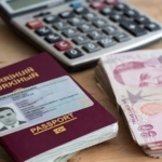 Pasaport, ehliyet ve Türk Lirası banknotları, arka planda hesap makinesi.