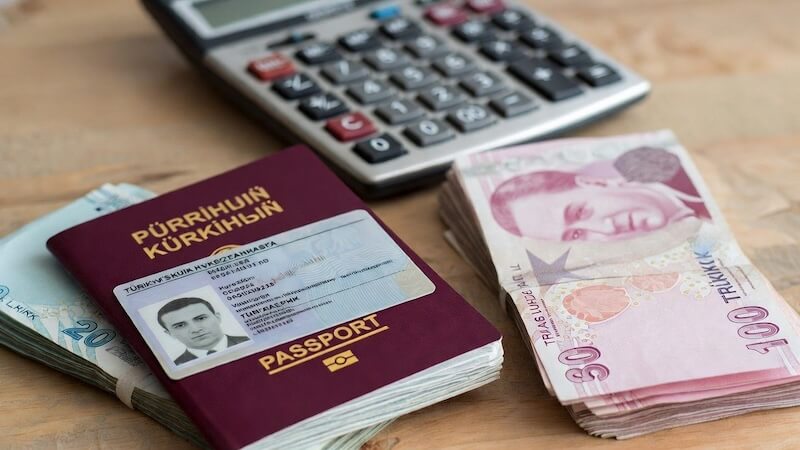 Pasaport, ehliyet ve Türk Lirası banknotları, arka planda hesap makinesi.